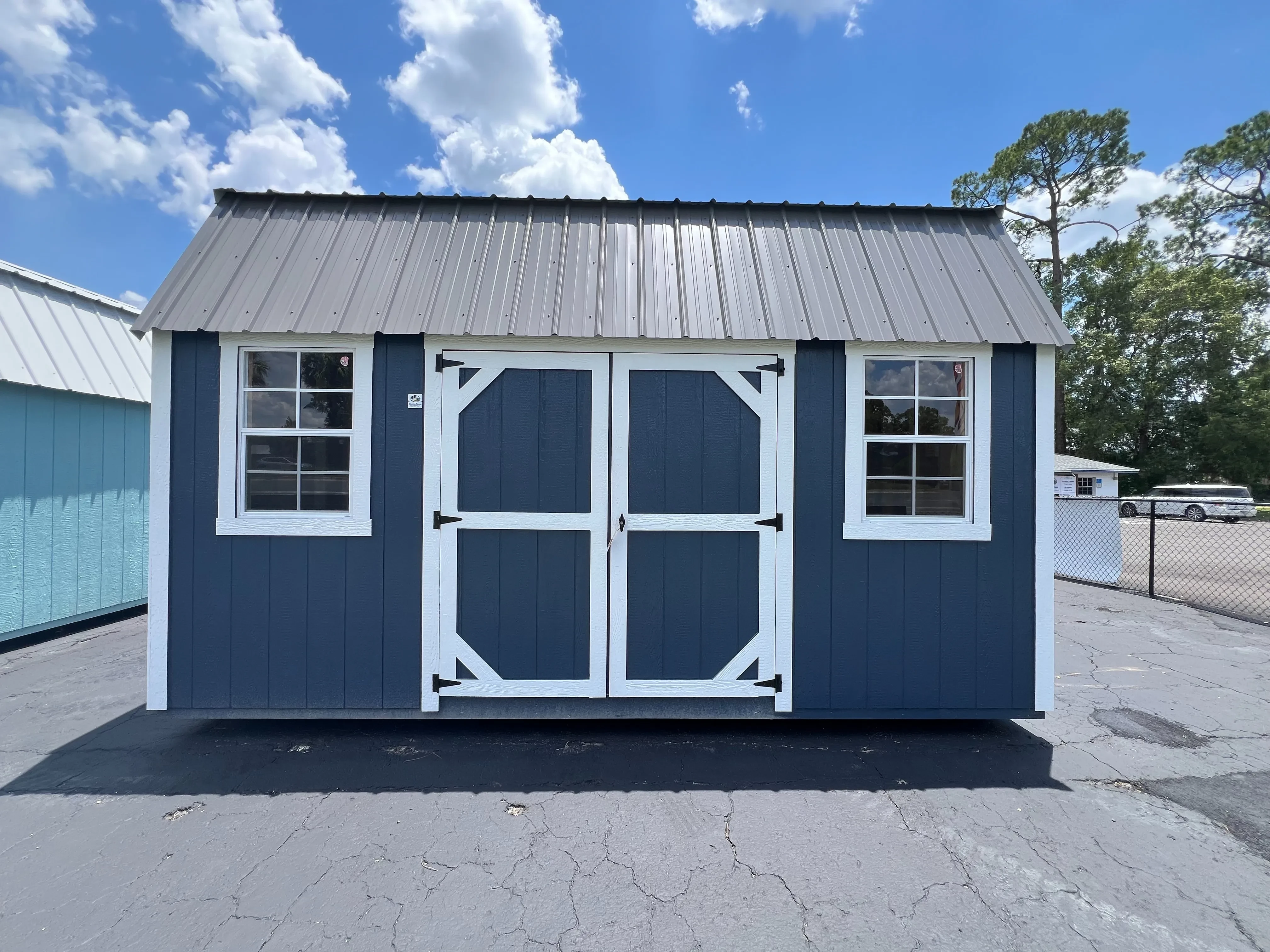 Outside of a 10x16 side lofted barn with double wood doors and two windows, painted wood side, and a metal roof.