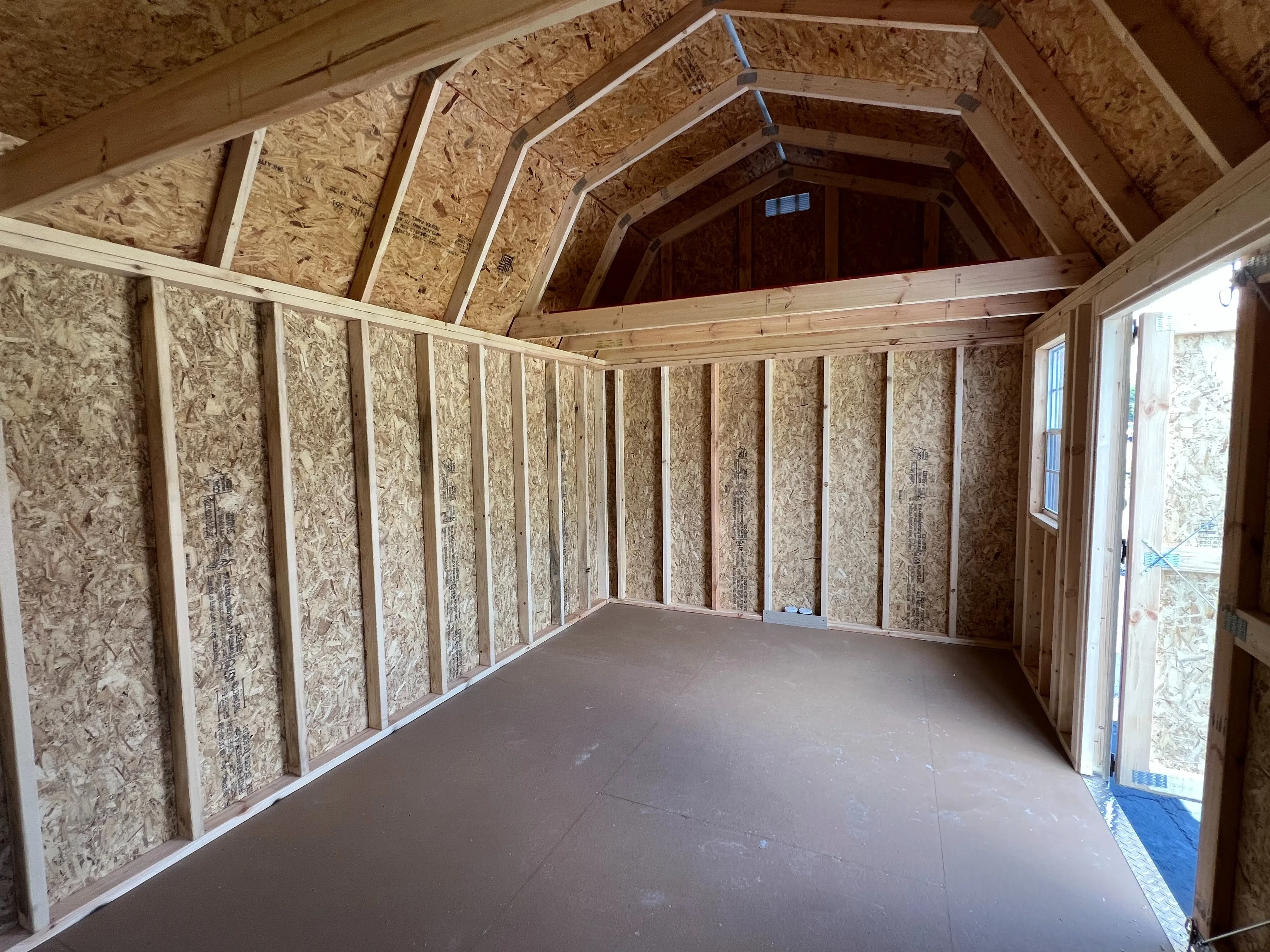 Interior of a 10x16 side lofted barn showing the inside of the double wood doors, a window, and a four foot loft in the end.