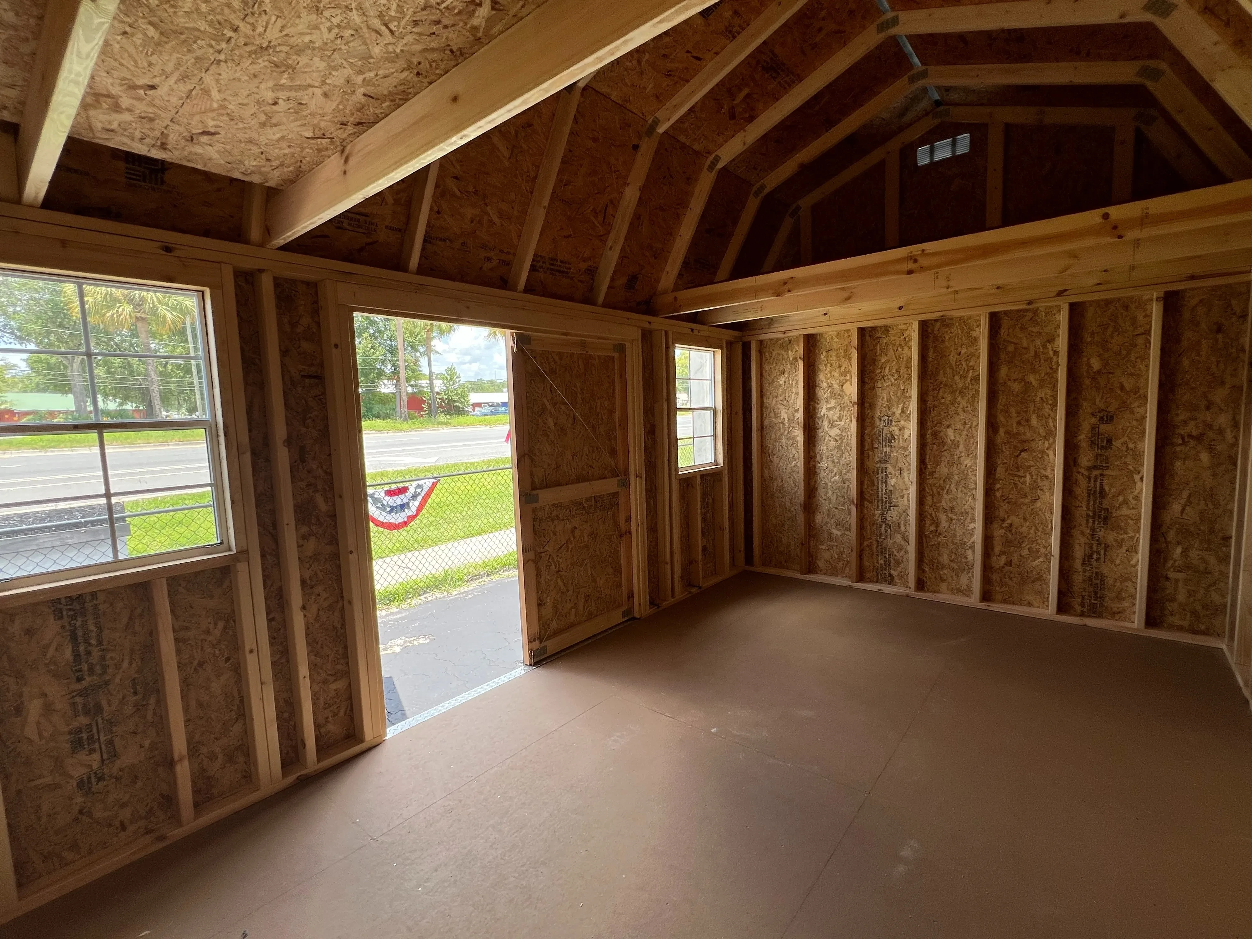 Interior of a 10x16 side lofted barn showing the inside of the double wood doors, two windows, and a loft in the end.
