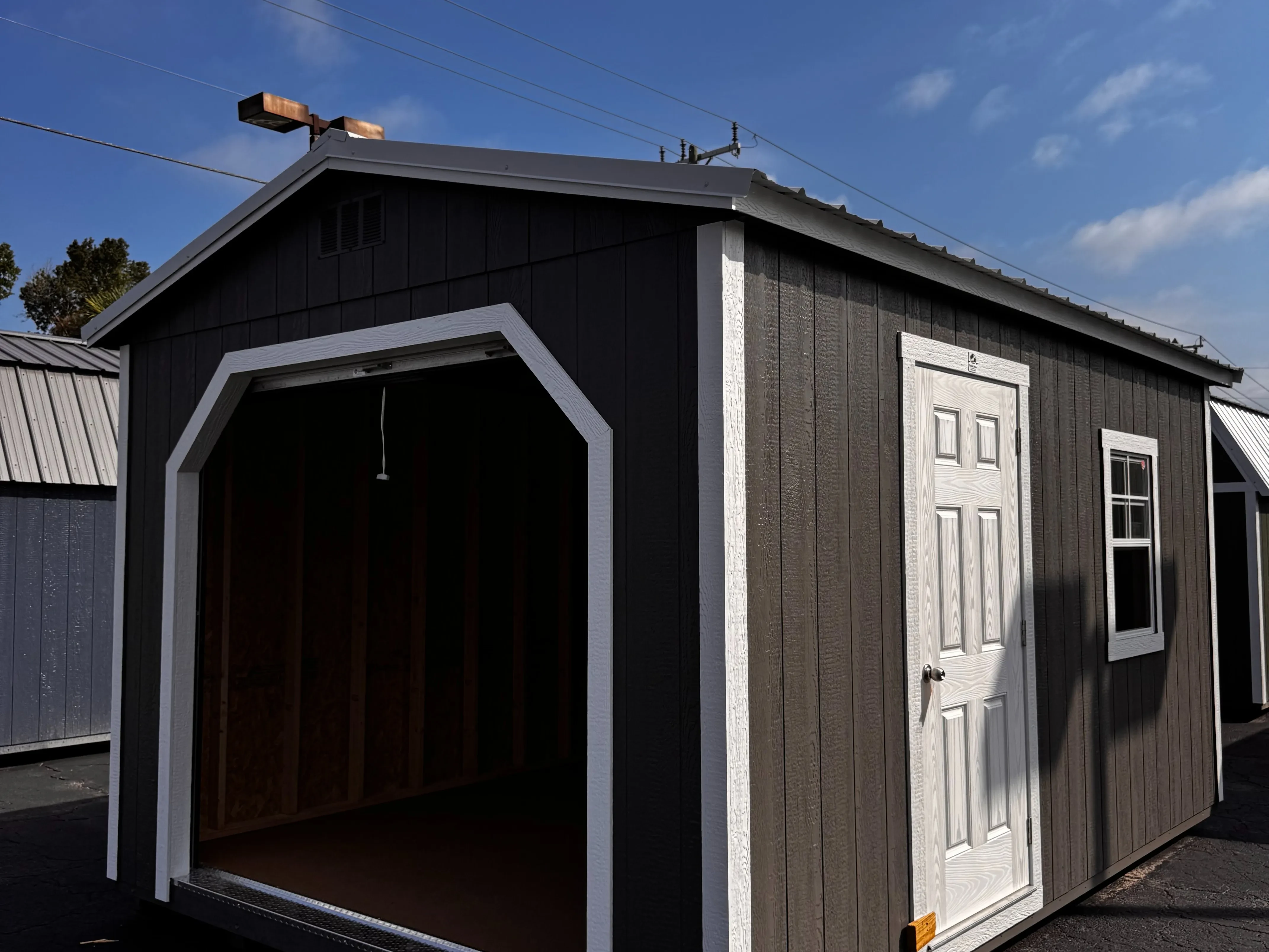 Exterior of a Charcoal Grey 12x16 workshop shed showing a garage door in the end, and a walk-in door and window on the side