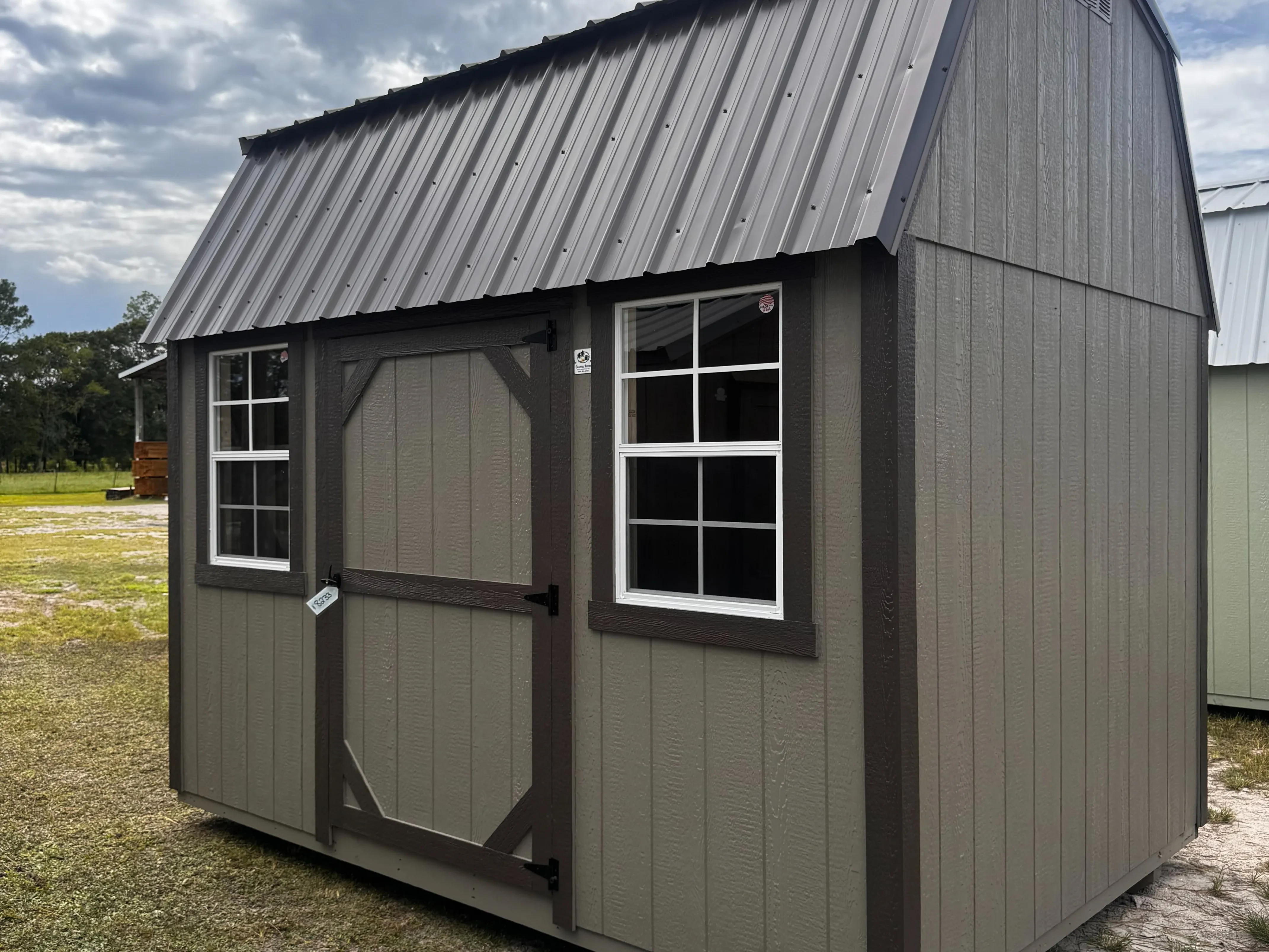 Exterior front right view of a metal clay 8x12 side lofted barn showing a wood door and 2 - 2x3 windows