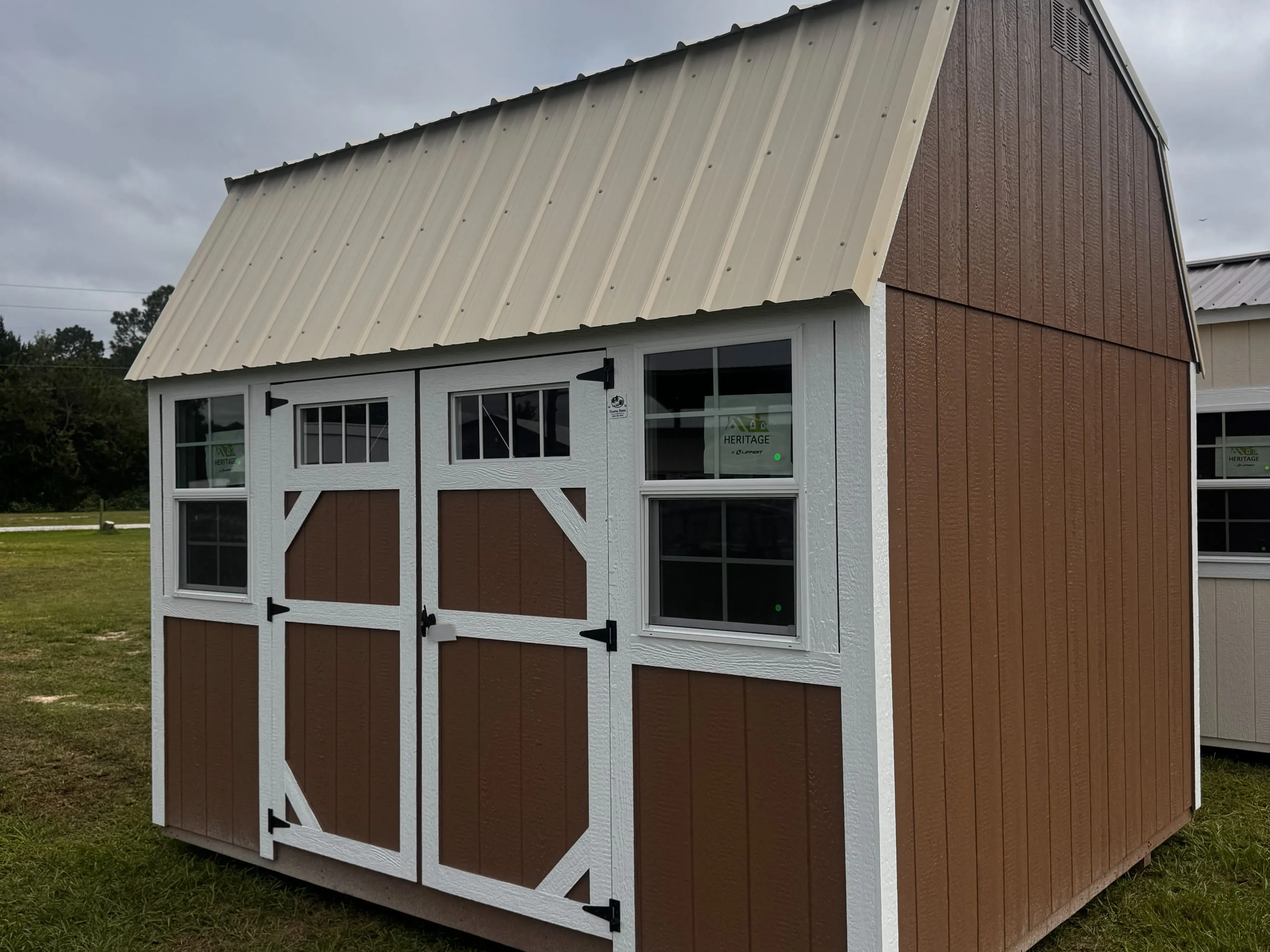 Exterior of a 10x12 side lofted barn with double wood doors with transom windows and two windows, painted wood side, and a metal roof.