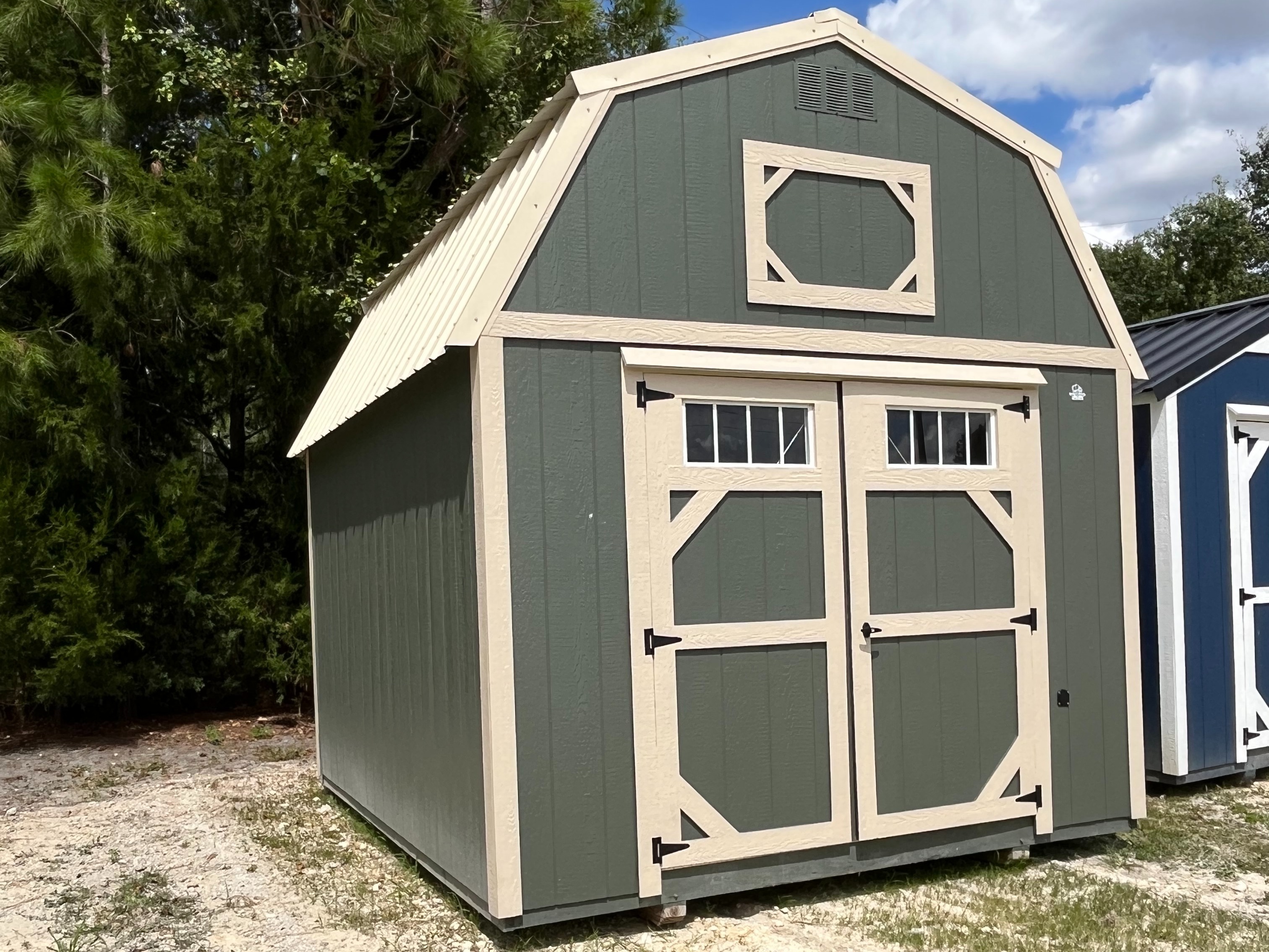 green lofted barn exterior front and right sides with tan trim and double doors with transom windows in the end of the shed