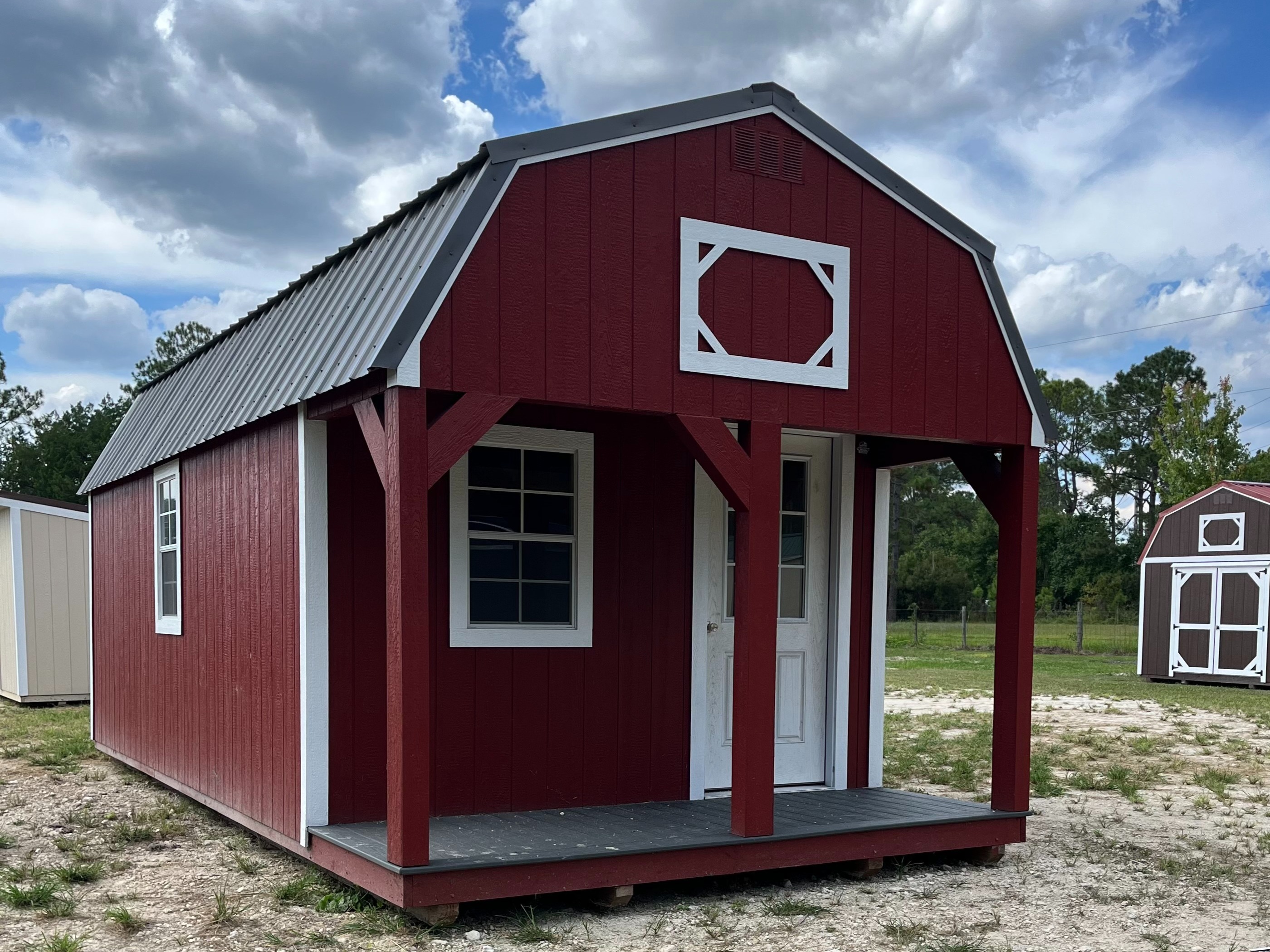 red lofted barn cabin with white trim, has a porch with a window and a walk-in door on the front