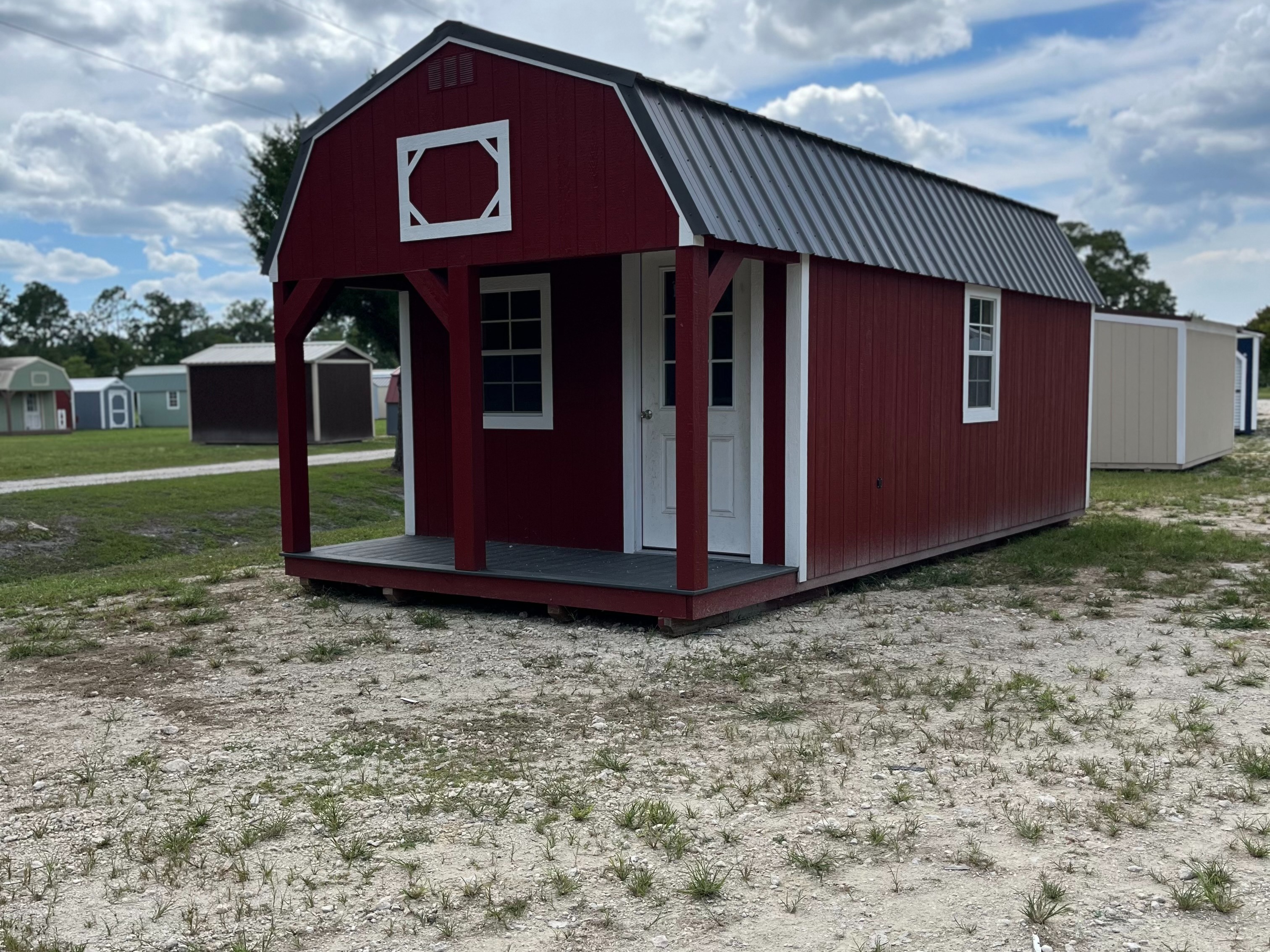 red lofted barn cabin with white trim, has a porch with a window and a walk-in door on the front