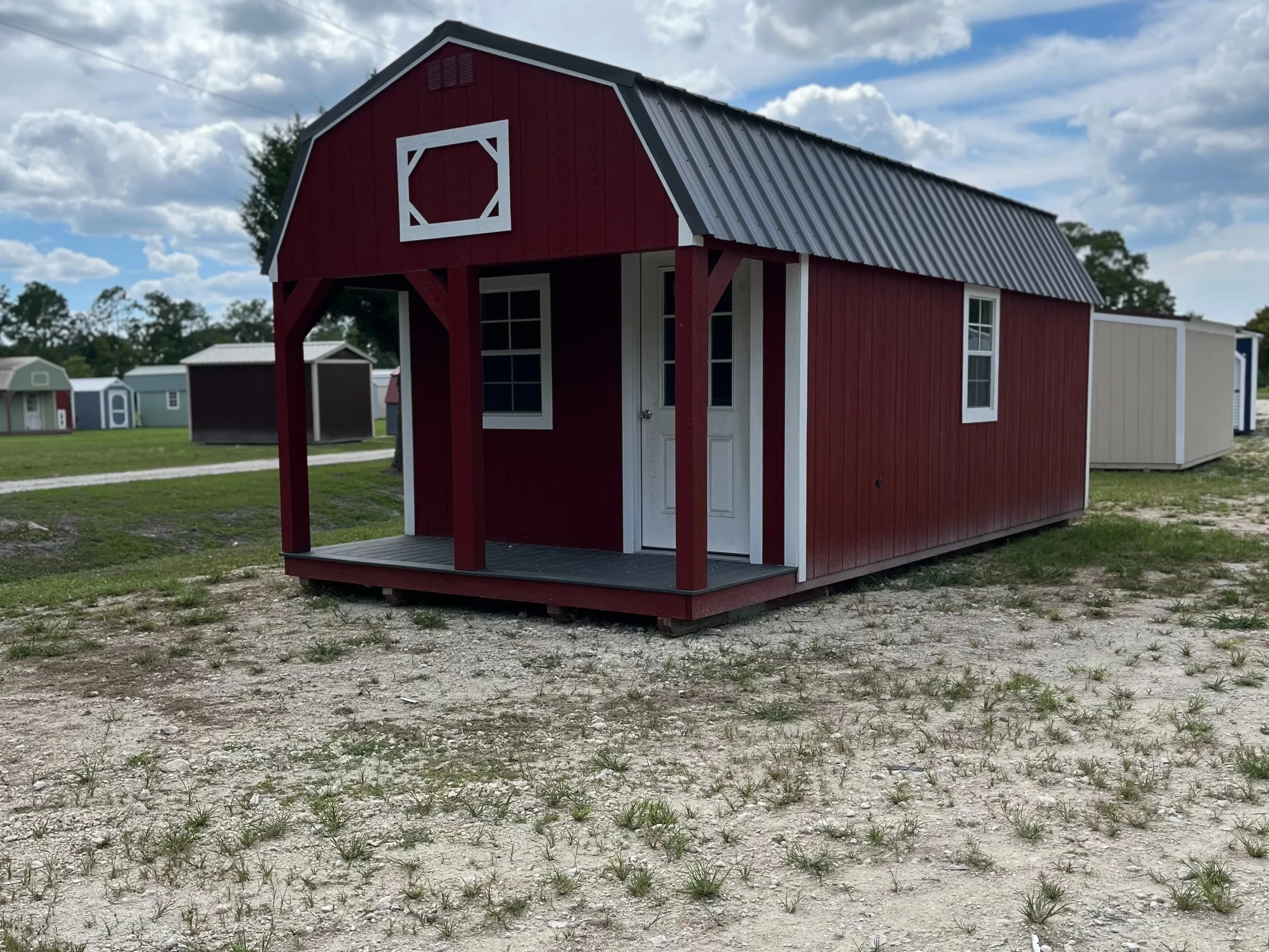 Red lofted barn cabin with white trim, has a porch with a window and a walk-in door on the front