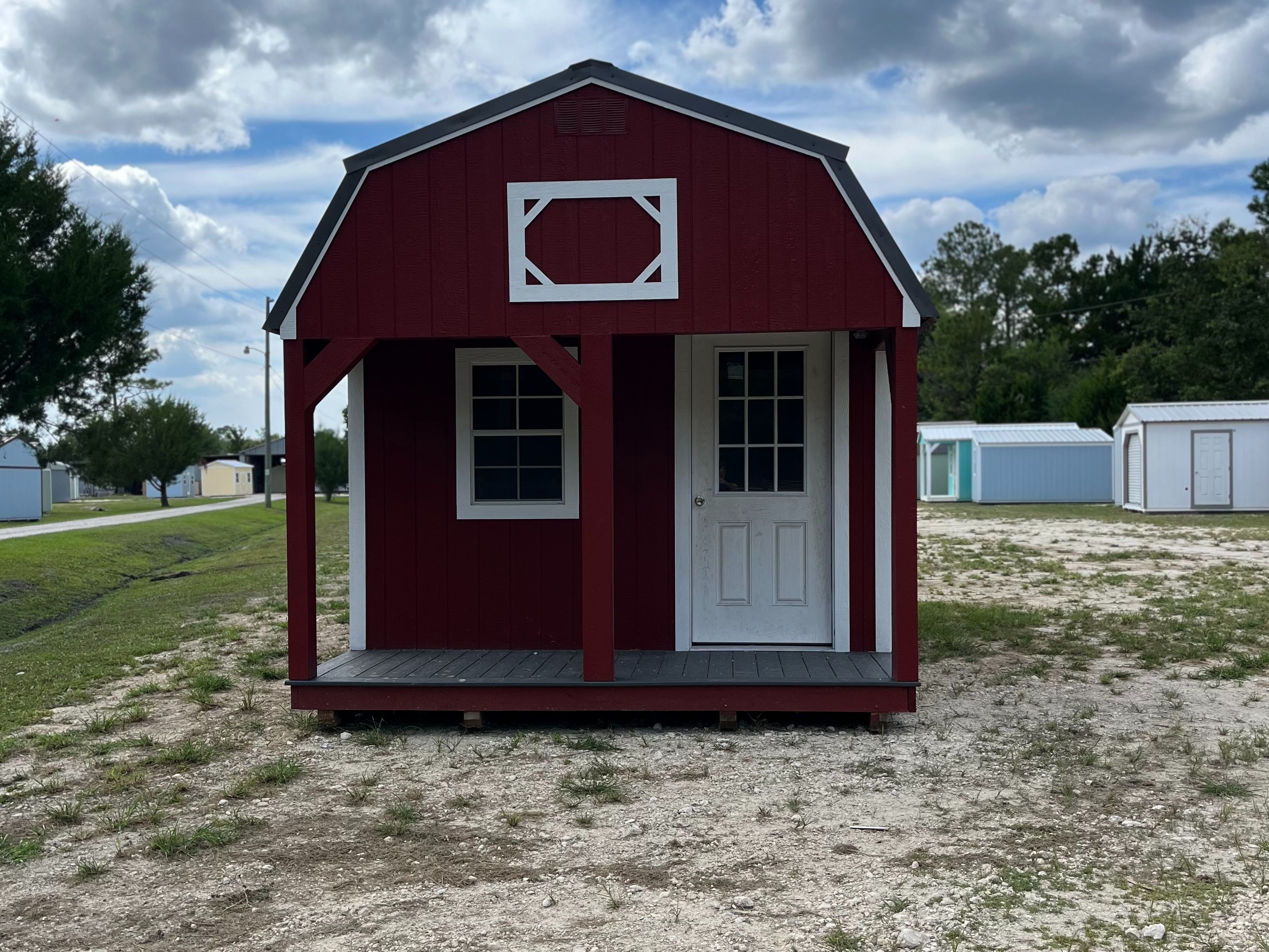 red lofted barn cabin with white trim, has a porch with a window and a walk-in door on the front