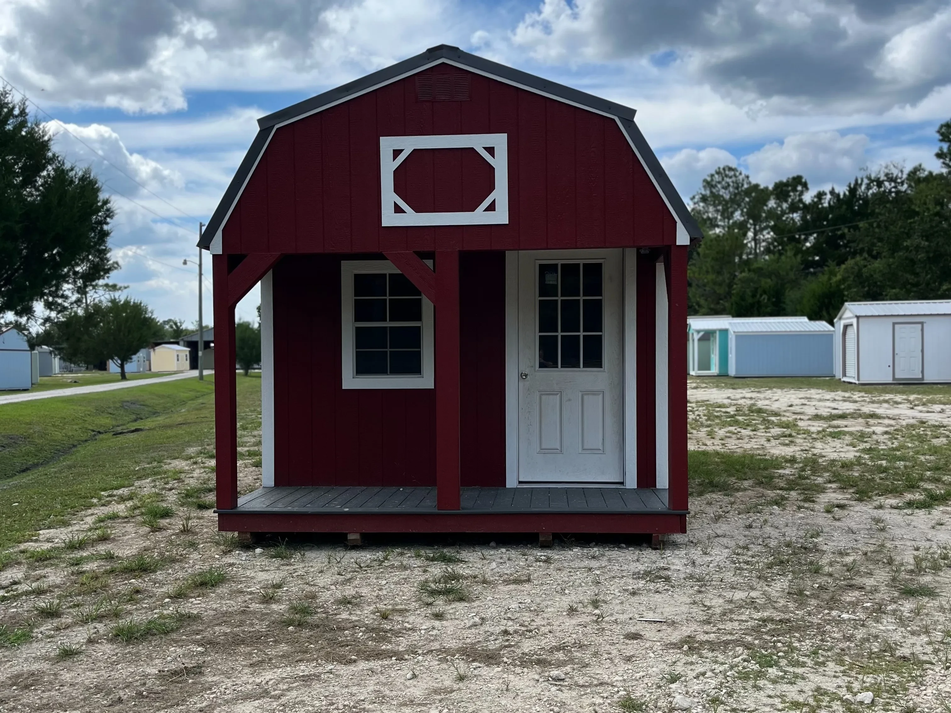 Red lofted barn cabin with white trim, has a porch with a window and a walk-in door on the front