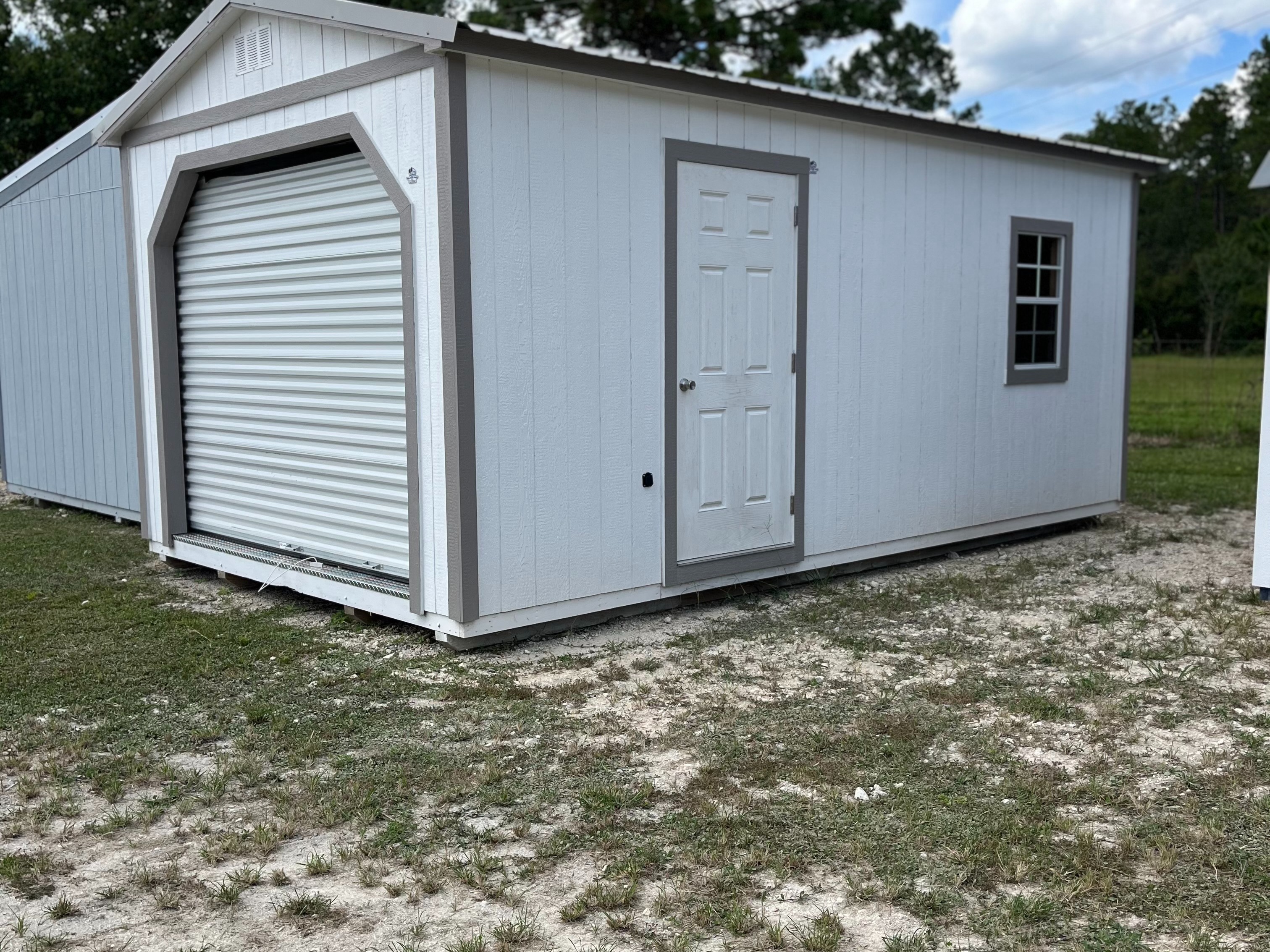 exterior of white workshop shed showing a garage door in the end, and a walk-in door and window in the side