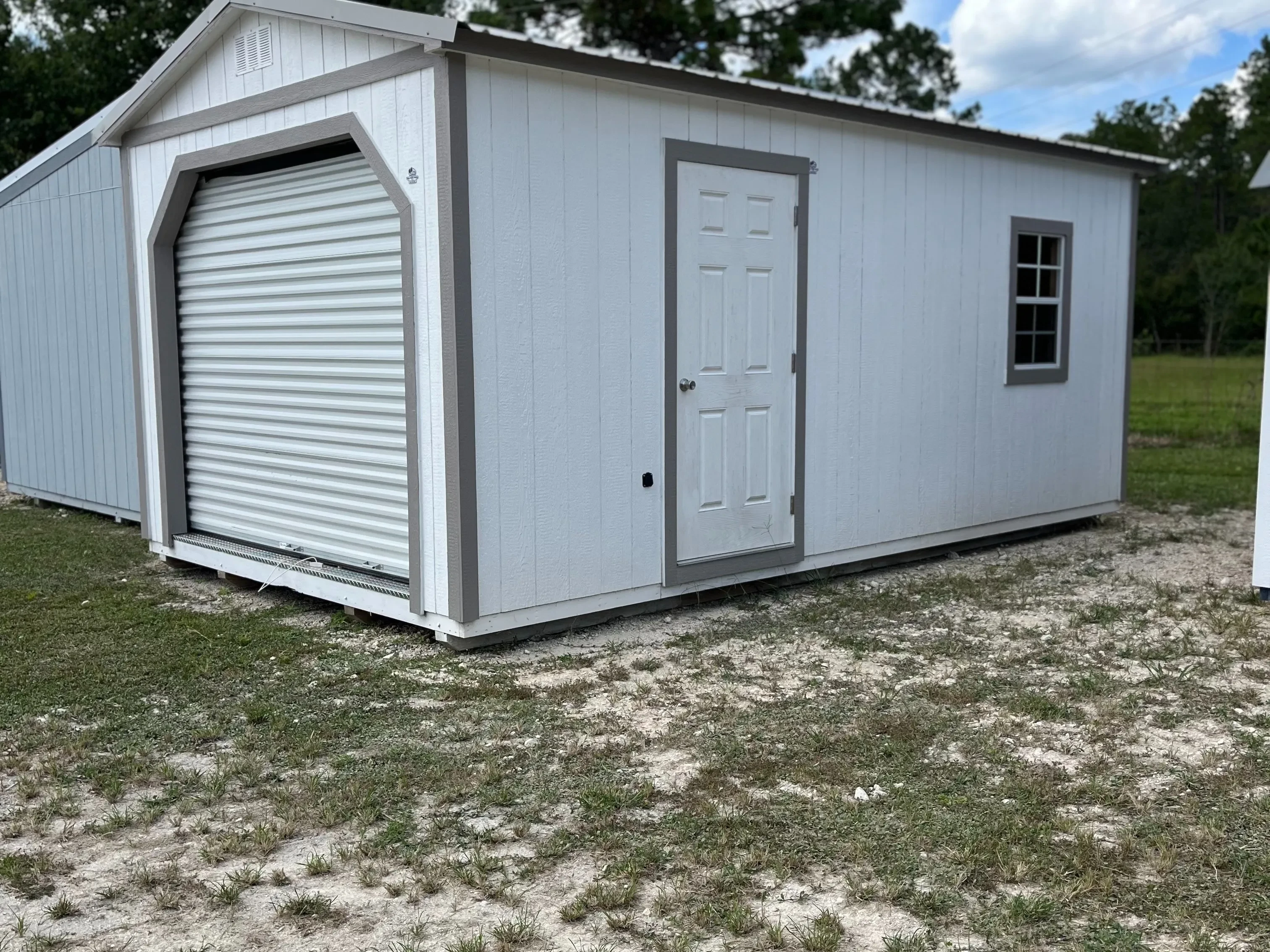 Exterior of white workshop shed showing a garage door in the end, and a walk-in door and window in the side