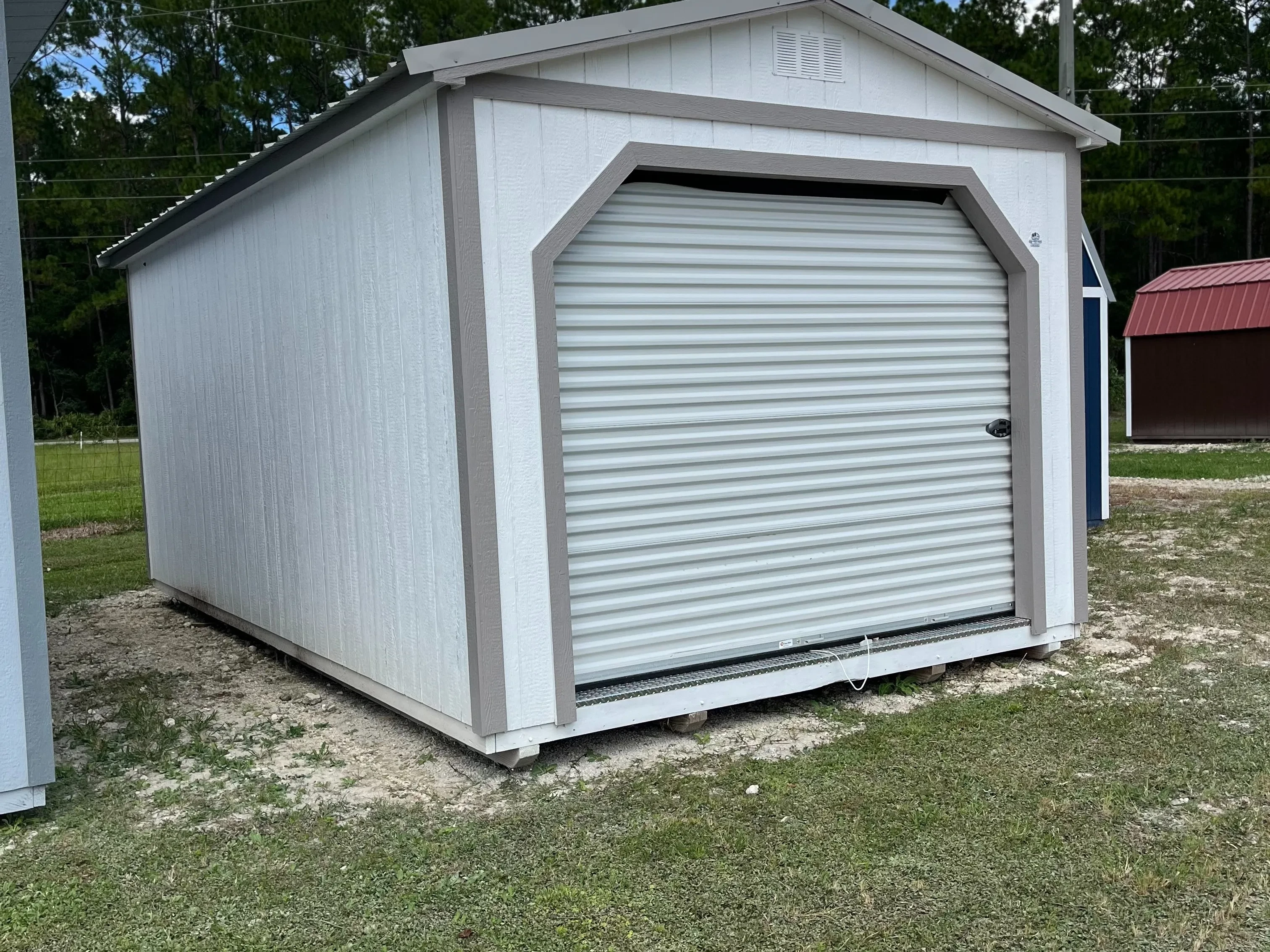 Exterior of white workshop shed showing a garage door in the end, and a solid wall