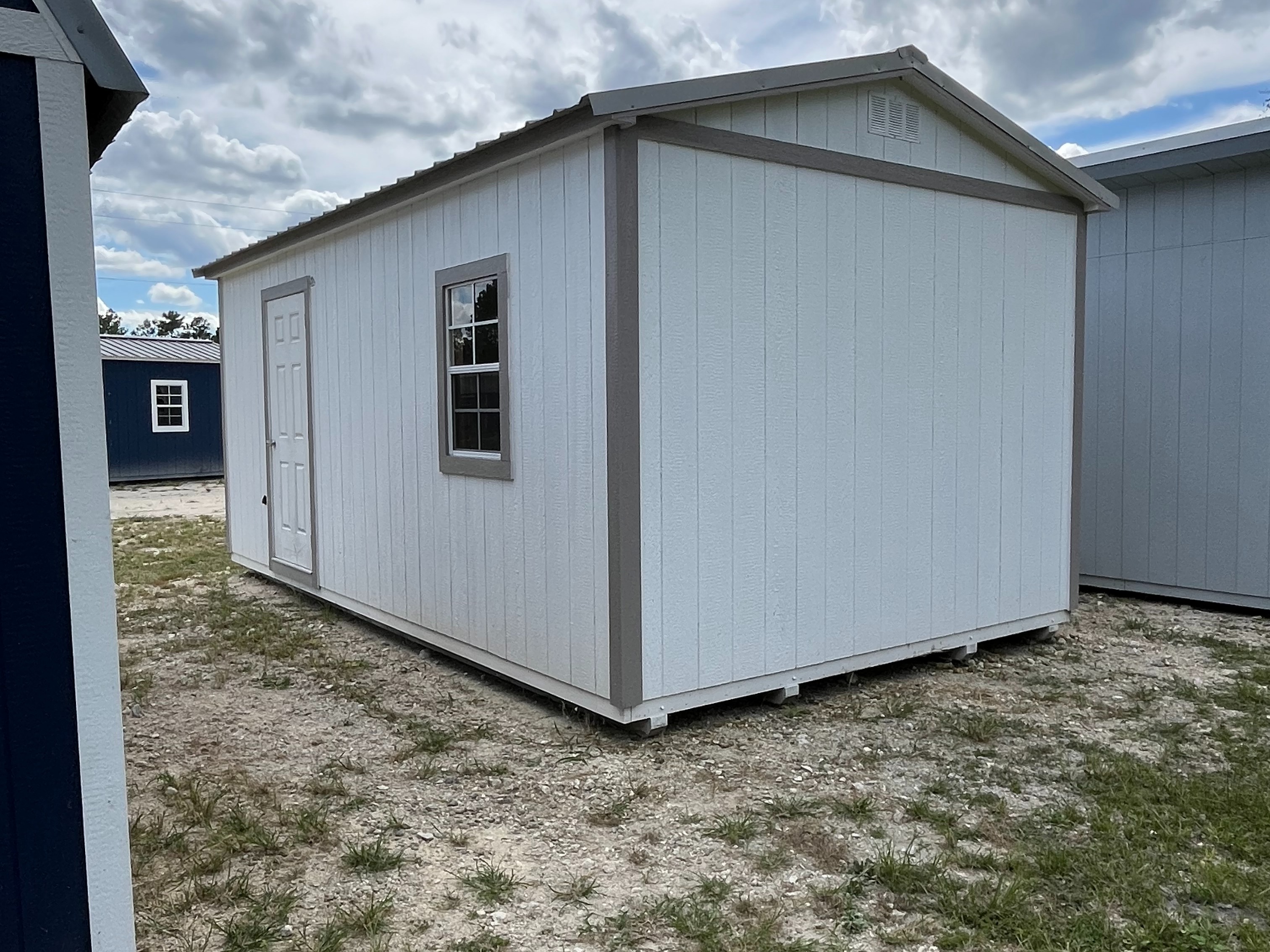 exterior of white workshop shed showing a garage door in the end, and a walk-in door and window in the side