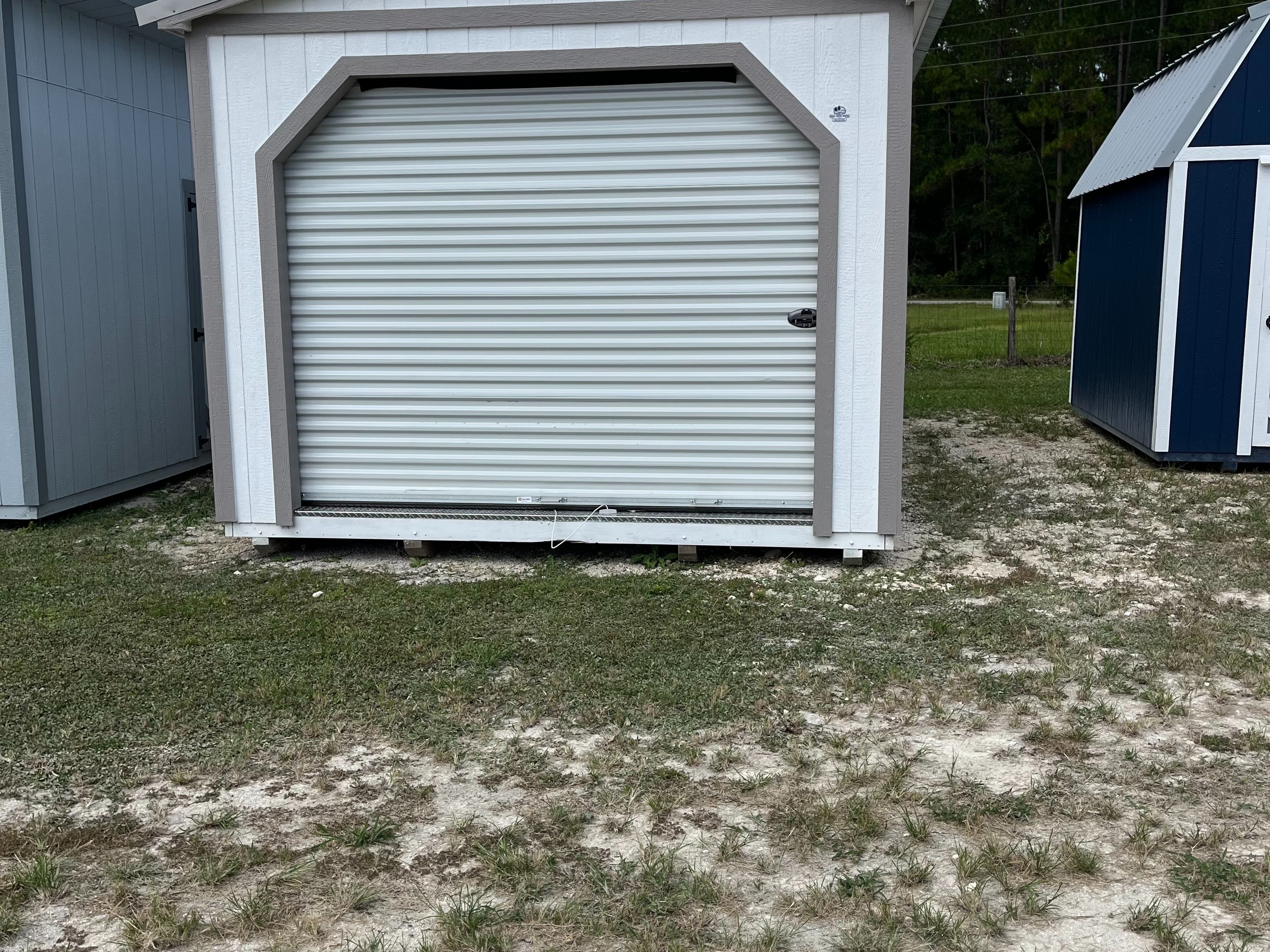 exterior of white workshop shed showing a garage door in the end, and a walk-in door and window in the side